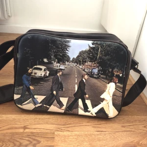 The Beatles väska - Säljer denna läder liknande/ bruna axelremsväska med the Beatles motiv! Köpt i Berlin men aldrig kommit till användning. Storlek - får plats en laptop i med mera! Mycket bra skick då oanvänd.