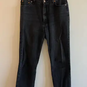 Svarta jeans med sliten kant längst ned. Färgen är lite åt det gråsvarta hållet.