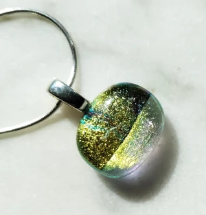 Hängsmycke i glas - Hängsmycke i två olika sorters guldfärgat glas och med silverpläterat hänge. Glaspärlan mäter ca 1,75 cm. Silverkedjan (925 Sterlingsilver) kan köpas separat.