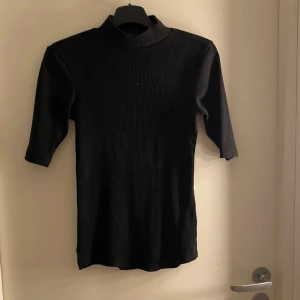 Tröja - Svart ribbad polotröja, sömmen nertill har gått upp lite (se bild 2) det går lätt att laga om man har en symaskin och vill annars syns det inte så tydligt. Vet ej märket. Okej skick.