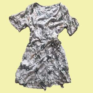 Somrig kort wrapklänning i ett grått blommigt mönster. Köpt för några år sedan men knappt använd så är i jättebra skick. 