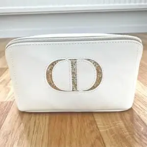 Christian Dior sminkväska i nytt skick och är oanvänd. Den är vit med en guldpaljetterad Dior logga. Gjord av PU-läder (artificiellt). Insidan är av ett skyddande material som är lätt att rengöra.  Var del av ett gåvoset. Originallådan medföljer.