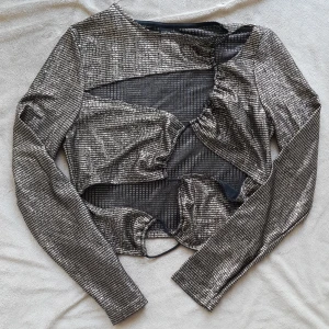 Topp - Snygg långärmad topp i svart och guld samt med cut-outs. Är något croppad och är något liten i storleken. Har aldrog blicit använd och är i nyskick.