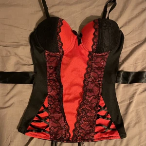 Topp  - En sorts korsett topp, sitter tight med föera snören på baksidan, äcen en liten dragkedja (går nt hela vägen ner) 