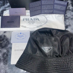 Prada bucket hat - Säljer nu min prada solhatt då det inte är något för mig. Gillade inte hur den satt på mig och nu vill sälja vidare den. Den är i bra skick skulle säga 8/10 storlek M färgen svart. Du får med alla tillbehör i bilderna :) 