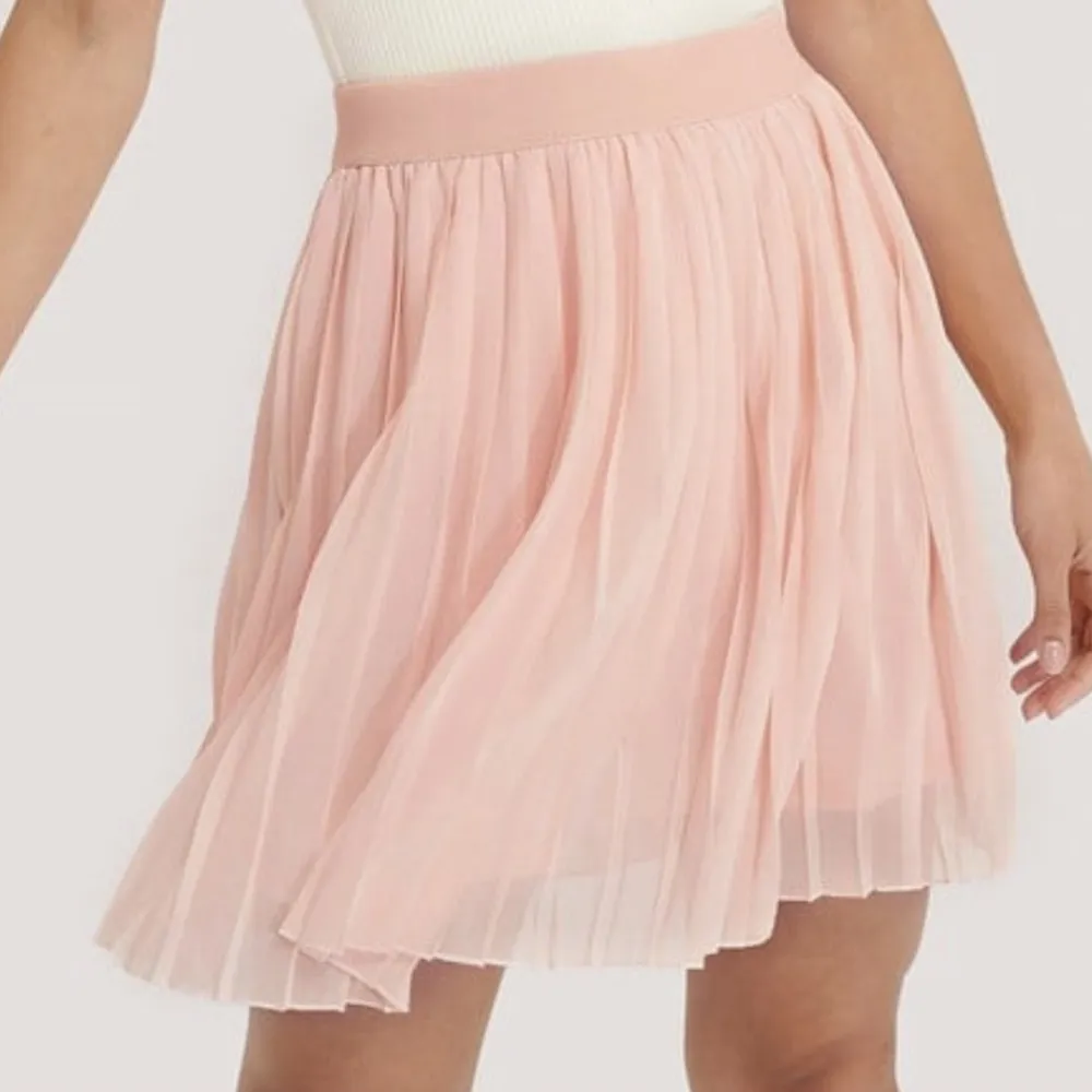 Veckad minikjol i storlek S från NA-KD. Rosa.  Den här kjolen har en minilängd, en veckad design, en resårmidja och en flowy fit. This skirt comes in light pink. Färgen är som på första bilden. Det är väldigt konstigt ljus på 2 och 3 Skriv för fler bilder. Kjolar.