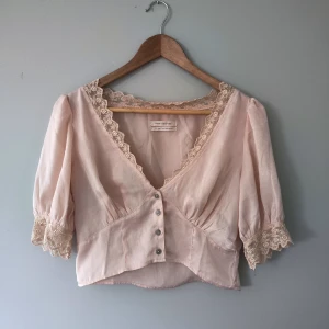 Ljusrosa topp med puffärmar - Fin topp med spetsdetaljer. Tyget känns väldigt lyxigt och glänser fint i solen. Den är lite mer persikofärgad än det ser ut på bilderna.