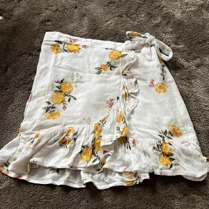  vit kjol med gula blommor på!  - Det är en fin vit kjol med gula blommor på, det finns några små rosa blommor på också. kjolen har 2 snören så du kan knuta den om det behövs. 🌼☀️🌸