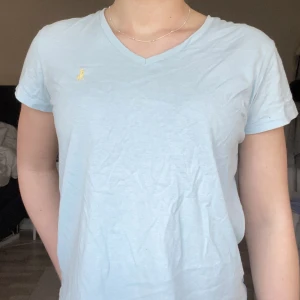 Blå t-shirt från Ralph Lauren - Så fin somrig t-shirt! Den är v-ringad och har ett gult märke på högra sidan. Har inte användning för den längre, men den är i bra skick!
