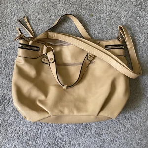 Väska med gulddetaljer  - Beige väska med gulddetaljer och hängen för accessoarer 💕 Nyskick ✨Man får plats med både mappar, skoldator och vattenflaska 💕 