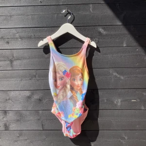 Elsa och Anna baddräkt - En Elsa och Anna baddräkt med regnbågens alla färger och med en liten rosett i ryggen.
