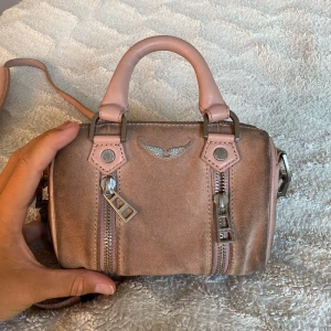 Zadig & Voltaire väska - Väska från Zadig & Voltaire. Väldigt använd därav priset. Väskan är i mocka och därav har skavt av på den baksidan av väskan