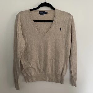 Långärmad Ralph Lauren - En långärmad tröja från Ralph Lauren i en fin beige färg. Använd vid ett fåtal tillfällen men är inte nopprig, den enda lilla defekten som finns är en liten söm som gått upp framtill i v-ringningen. Går säkert att laga med lite nål och tråd!