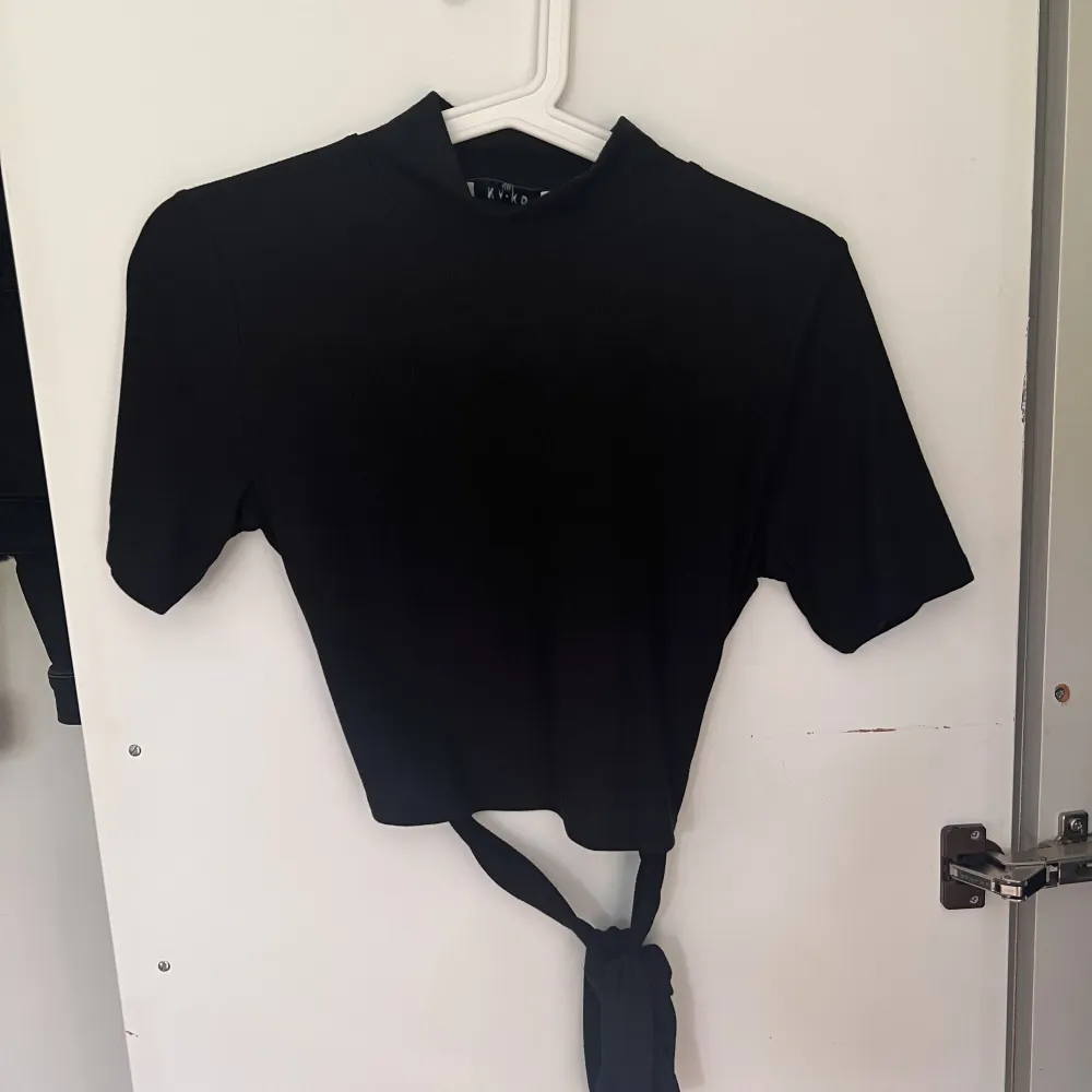En svart t-shirt med öppen rygg,  knytning längst ner och hög krage. Använd ett fåtal gånger. Storlek M. Från NA-KD. T-shirts.