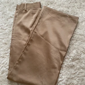 Champagne byxor  - Finbyxor från NA-KD i en champagne guldig blank färg! Säljer de för de är tyvärr alldeles för stora och långa på mig. Tyvärr någon liten fläck men har inte testat tvätta de, annars fint skick. 