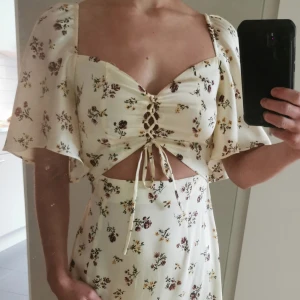 Somrig klänning - Somrig maxiklänning med blommotiv. Knytdetalj, utskuret parti, sidoslits.  Nyskick - aldrig använd. Prislapp kvar.   Storlek XS/34