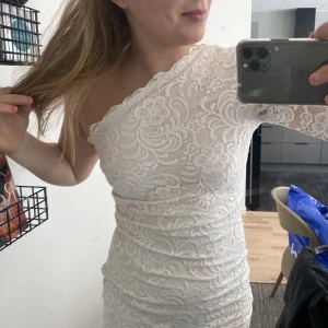Klänning spets - Gammal goding från bubbleroom som nu är till salu. Endast använd en gång på konfirmation (se bilder), men funkar också till student eller skolavslutning. Vit spetsklänning med en ärm och sne skurning tvärs över bröstet.