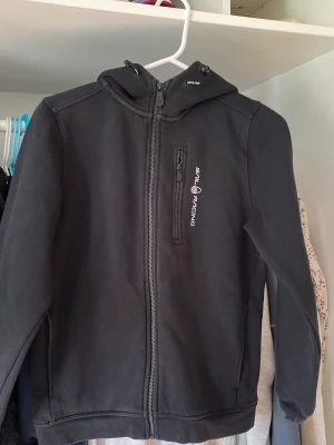Sail racing huvtröja - Svart huvtröja från sailracing. Andvänd ett fåtal gånger. Väldigt bra skick. Storlek 160. Ny kostar runt 1000kr. Tveka inte att höra av dig om du undrar över något