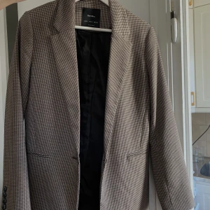 Hundtandsmönstrad kavaj - Superfin brunbeige kavaj i hundtandsmönster. Har en reva i innerfodret men inget som syns på utsidan. 