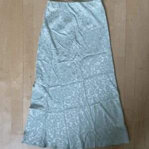 Mintgrön långkjol - Långkjol i blommigt satintyg från bikbok. Kjolen har resor i midjan och en kort slits längst ned. Kjolen är väl omhändertagen och i mycket bra skick.