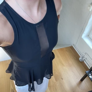 Svart fest topp - En super snygg fest topp. Svart rygg med see throw framtill. Öppen i ryggen, med en knapp upp till och sedan dragkedja från midjan och ner. Volanger ner till. Sparsamt använd!