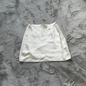En NA-KD kjol i strorlek 36. Vit shimrig färgad men mer åt de vita hållet.