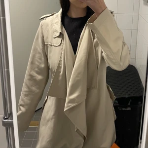 Kappa Veromoda  - Fin tunn beige kappa från Vero Moda i storlek M, jackan har ett bälte som gör att den kan stylas o bäras på flera sätt! Inga hål eller defekter.