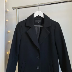 Klassisk kappa - Klassisk svart kappa i nyskick, använd endast ett fåtal gånger⭐️ Perfekt för höst, vinter och vår!  Tre knappar i fram, observera att endast knappen i mitten är knäppbar.   34% Ull 59% Polyester 4% Akryl 3% Andra fibrer 