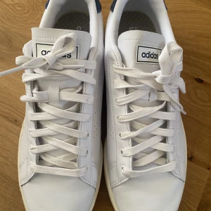 Adidas Advantage strlk 46 i nyskick  - Adidas Advantage i vitt med blå mockadetalj baktill. Perforerade 3-Stripes. Cloufdfoam innesula gör dem sköna att gå i. Använda ett fåtal gånger, som nya!