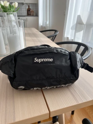 Supreme Waistbag FW17 Reflective Logo - Waistbag från Supreme från FW17-kollektionen. Väskan är av Cordura Fabric och har en box logo samt logotyp i reflex på undersidan.  Har använts en del, därav lite slitage (se sista bilden). Cond:7/10  Lowest ask på StockX: $279