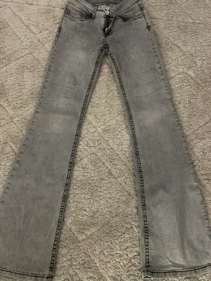 Grå bootcut jeans med hög midja - Säljer ett par grå bootcut jeans med hög midja och dubbla knappar framtill. Jeansen har en tvättad look och utsvängda ben, perfekta för en trendig och avslappnad stil. Klassiska fickor fram och bak. Liten fläck på sidorna❤️