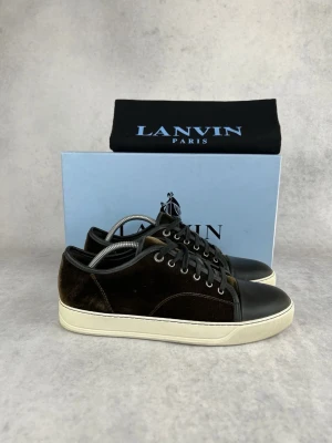 Lanvin svarta sneakers i mocka - Snygga svarta sneakers från Lanvin med ovandel i mjuk mocka och tåparti i slätt läder. Skorna har vita sulor och svarta skosnören. Klassisk låg modell med stilren design och exklusiv känsla. Perfekta för dig som gillar lyxiga detaljer.