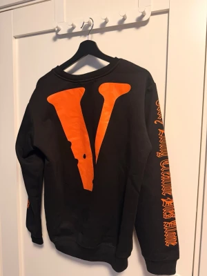 OFF-WHITE x Vlone sweatshirt - Svart sweatshirt från Vlone med stor orange V-logga på ryggen och orange text längs ena ärmen. Framtill står det 'OFF' i orange. Tröjan har rund hals och långa ärmar. Perfekt för dig som gillar streetwear och vill sticka ut.