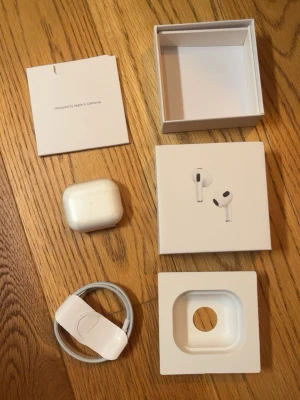 Apple AirPods 3 med laddningsetui - Säljer ett par vita Apple AirPods 3 med trådlöst laddningsetui och originalförpackning. Hörlurarna har en stilren och kompakt design i plast, och medföljer gör även en USB-C till Lightning-kabel. Perfekta för musik, samtal och träning. Helt nya oöppnade.