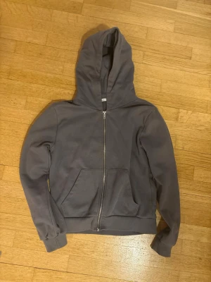 Grå zip hoodie med fickor - En stilren grå hoodie med dragkedja framtill och två stora magfickor. Hoodien har ribbade muddar vid ärmslut och nederkant samt en klassisk huva. Perfekt för en avslappnad look och enkel att matcha med andra plagg. Storlek xs. Priset går att diskutera. Frakt ingår ej! Använd fåtal gånger.