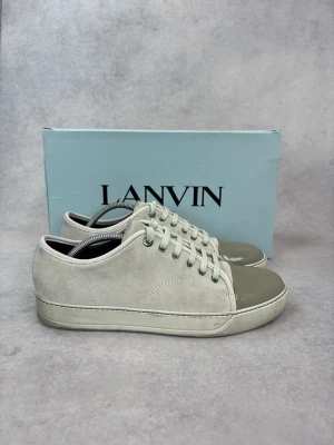 Lanvin sneakers i mocka och lack - Snygga sneakers från Lanvin i ljusbeige mocka med gråbeige lackad tå. Klassisk låg modell med vita snören och diskret sömnad. Perfekta för dig som gillar stilrena och exklusiva sneakers med en twist.