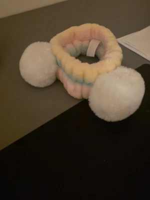 Pastellfärgat fluffigt hårband - Supersött hårband i mjuk, fluffig plysch med stora vita bollar på sidorna. Bandet har pastellfärger i gult, rosa och blått. Aldrig använd 