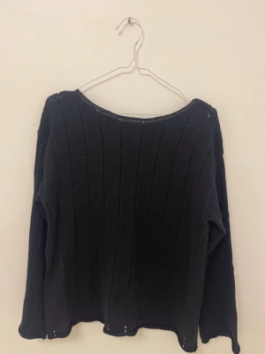 Svart stickad tröja med hålmönster - En svart stickad tröja med lång ärm och dekorativa hålmönster i vertikala rader. Tröjan har en rund halsringning och en något loose passform. Enkel och stilren design som passar till det mesta. Kan användas som en beach cover-up. Strl 150 och passar dig med XS/S