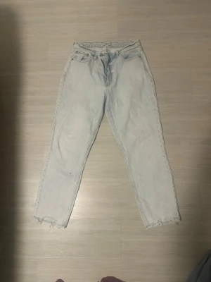 Ljusblå mom jeans med råa kanter från Abercrombie and Fitch - Säljer ett par ljusblå mom jeans med hög midja och raka ben. Jeansen har råa, fransiga kanter vid bensluten och klassisk femficksdesign. Perfekta för en avslappnad och trendig look. Finns en svag fläck på vänster knä. Stl 29/32