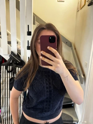 Mörkblå stickad kortärmad tröja - Snygg mörkblå stickad tröja från Kappahl med korta ärmar och rund halsringning. Tröjan har ett klassiskt kabelstickat mönster framtill och är något croppad i modellen. Perfekt för en trendig och avslappnad look.