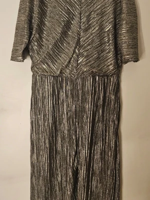 Glittrig metallic minidress med v-ringning - Säljer en snygg minidress i metallic silver med glittrig finish. Den har korta ärmar, v-ringning och plisserad struktur. Materialet är stretchigt och skimrande, perfekt för dig som vill sticka ut. Från Mango