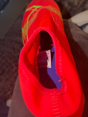 Nike Mercurial röda fotbollsskor - Säljer ett par Nike Mercurial fotbollsskor i en riktigt snygg röd färg med gröna detaljer. Skorna har en strumpliknande passform och är tillverkade i syntetmaterial för bästa grepp och känsla på planen. Perfekta för dig som vill sticka ut på fotbollsplanen. Använt ca 3 gånger på konstgräs men inte kommit till användning på flera år