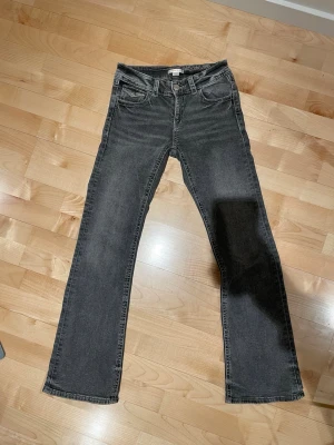 Grå bootcut jeans med broderade fickor - Snygga grå bootcut jeans med dekorativa broderier på bakfickorna och silvriga knappar. Jeansen har klassisk femficksmodell och är tillverkade i denim med lätt tvättad look. Perfekta för en avslappnad och trendig stil.