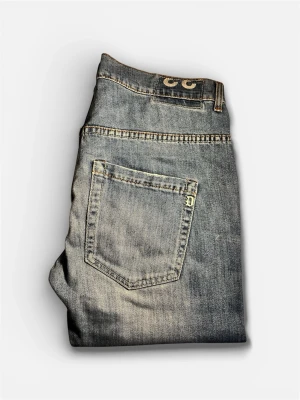 Blå Donudups med raka ben - Snygga blå Dondups med raka ben och klassisk femficksdesign. Jeansen har en lätt tvättad look med slitningar och synliga sömmar. Tillverkade i denim, perfekta för en avslappnad stil.