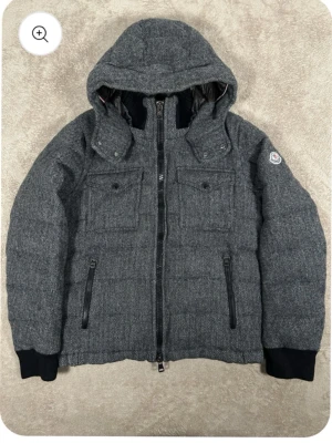 Moncler jacka florian  - Snygg grå dunjacka från Moncler med avtagbar huva och två bröstfickor med knappar. Jackan har svarta ribbade muddar vid ärmsluten och dragkedja framtill. Yttermaterialet har ett diskret fiskbensmönster och innerfodret är glansigt och quiltat för extra värme. ÄKTA!, kvittot finns! Storlek M men passar till både M och S 