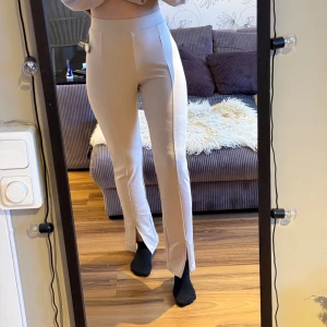 Kostymbyxor med slits - Säljer ett par oanvända beigea kostymbyxor med hög midja och raka ben. Stretchiga byxor med slits på framsidan. Storlek small