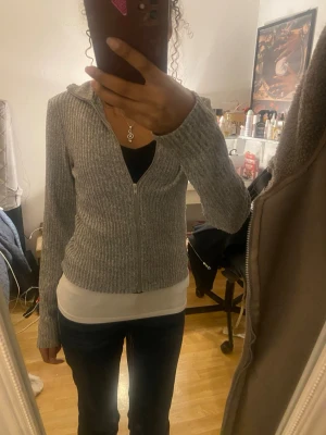 Grå ribbad kofta med dragkedja XS - •Säljer en grå ribbad kofta från Lager 157 i storlek XS. Koftan har lång ärm, hög krage och hel dragkedja framtill. Materialet är stickat och känns mjukt mot huden. Perfekt för lager-på-lager under kyliga dagar !!•