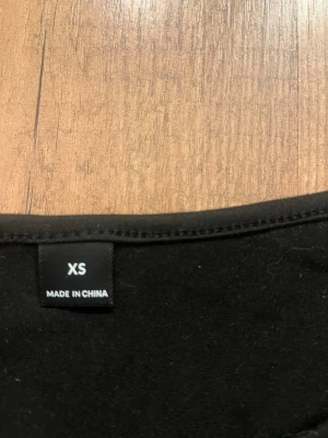 Svart linnetopp med smala axelband - Enkel och stilren svart linnetopp med smala axelband och lätt rynkning vid halsringningen. Perfekt att matcha med jeans eller kjol för en clean look. Tillverkad i mjukt material som känns skönt mot huden.