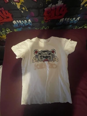 Vit Kenzo t-shirt med tigertryck - Vit t-shirt från Kenzo med ikoniskt tigertryck och logga framtill. Klassisk rund hals och korta ärmar. Perfekt för dig som vill sticka ut med en streetstyle-look.