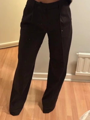 Bruna kostymbyxor från Filippa K - Snygga bruna kostymbyxor från Filippa K med raka ben och pressveck. Klassisk design med fickor fram och hällor för skärp. Perfekta för en stilren look och passar till många olika outfits.